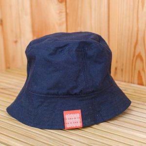 A navy blue bucket hat with a red rectangular patch sits on a light wooden surface with a wood-panelled background.