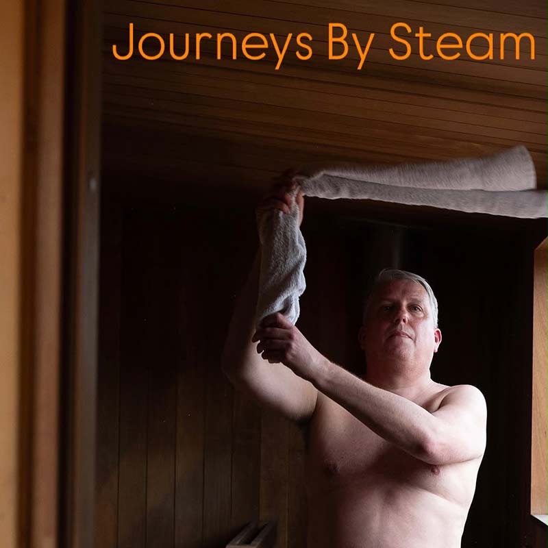 A bare-chested man stands in a wooden sauna, waving a towel near the ceiling. The text “Journeys By Steam” appears at the top.