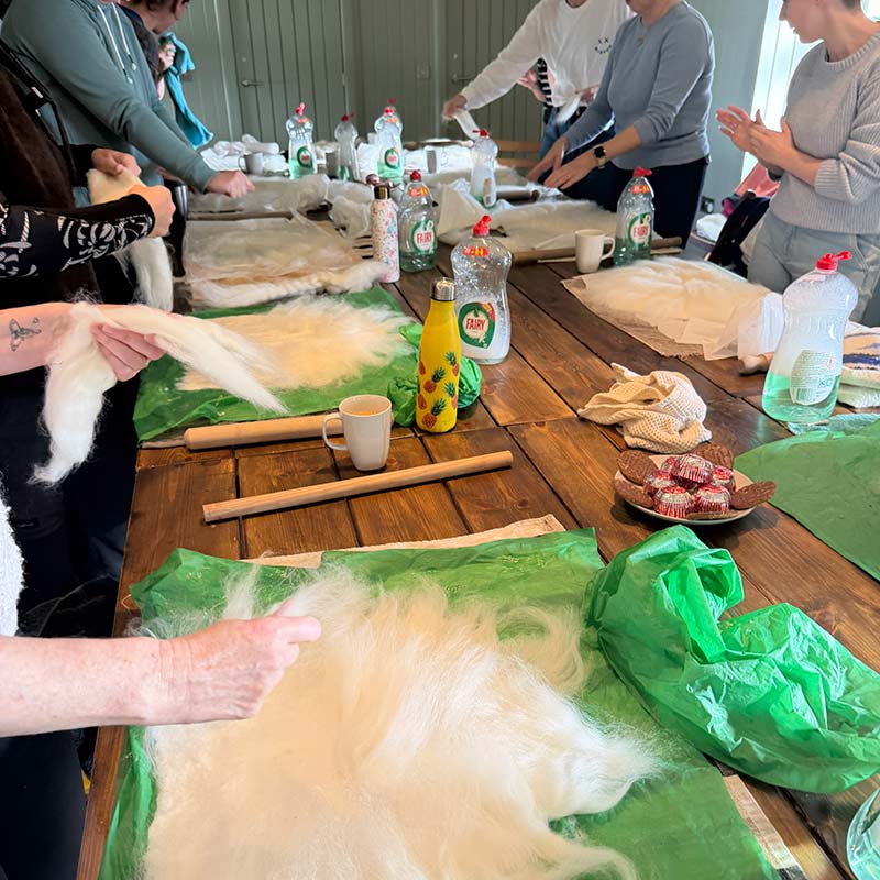 Sauna-hat-making People working on wet felting projects with wool tops and washing-up liquid at a long wooden table.